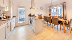 Une cuisine moderne avec des meubles blancs, un îlot central et un coin repas comprenant des chaises et une table en bois.