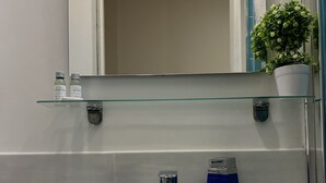 A bathroom with a white sink, two blue glass containers, a small potted plant, and a glass shelf above the sink.