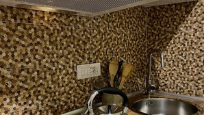 A kitchen with a stainless steel kettle on an induction cooktop, a sink, and a backsplash with hexagonal tiles.
