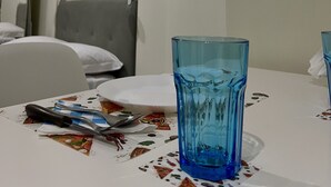 A hotel room with a bed, a table with a blue glass, and a painting on the wall.