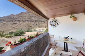 A balcony with a stone wall, a table with chairs, a wine glass, and a potted plant. - Vv Casa Frasquita. Fataga (Fataga)