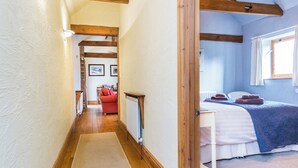 A narrow hallway with wooden beams, a radiator, a red sofa, and a bed with a blue blanket. - 2 bedroom accommodation in Louth (Louth)