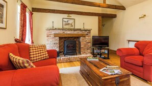 A living room with a fireplace, red sofas, a wooden coffee table, and a television. - 2 bedroom accommodation in Louth (Louth)