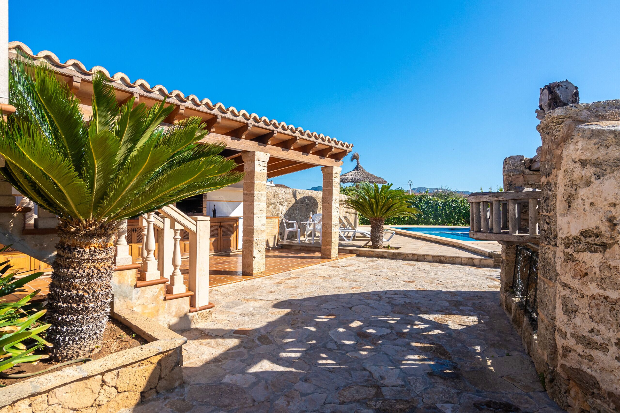 A stone patio with a pergola, palm trees, and a pool area.
