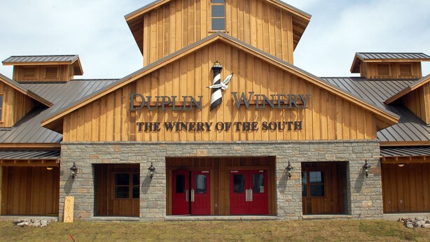 A winery building with a wooden facade, two red doors, and a sign reading "Duplin Winery - The Winery of the South".