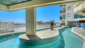 A swimming pool with a curved design, surrounded by a white fence, and a building with balconies in the background.