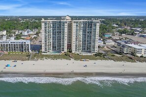 Un hôtel de grande hauteur, avec de nombreux étages, une plage au premier plan et un paysage urbain en arrière-plan.