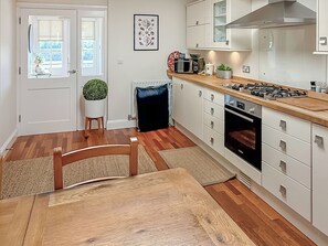 A modern kitchen with white cabinets, a wooden countertop, a stove, and a microwave. - The Police Station - UK45642 (Silloth)