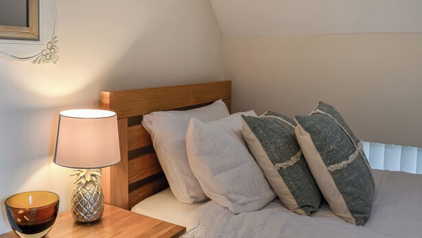 A bedroom with a wooden headboard, a bedside table with a lamp and a bowl, and a bed with multiple pillows. - The Police Station - UK45642 (Silloth)