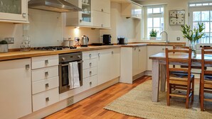 A modern kitchen with a central island, built-in appliances, and a dining area with wooden chairs. - The Police Station - UK45642 (Silloth)
