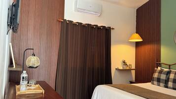 Ein Hotelzimmer mit einem Bett, einem Schreibtisch mit Lampe, einer Wasserflasche und einem kleinen Tisch mit Pflanze.