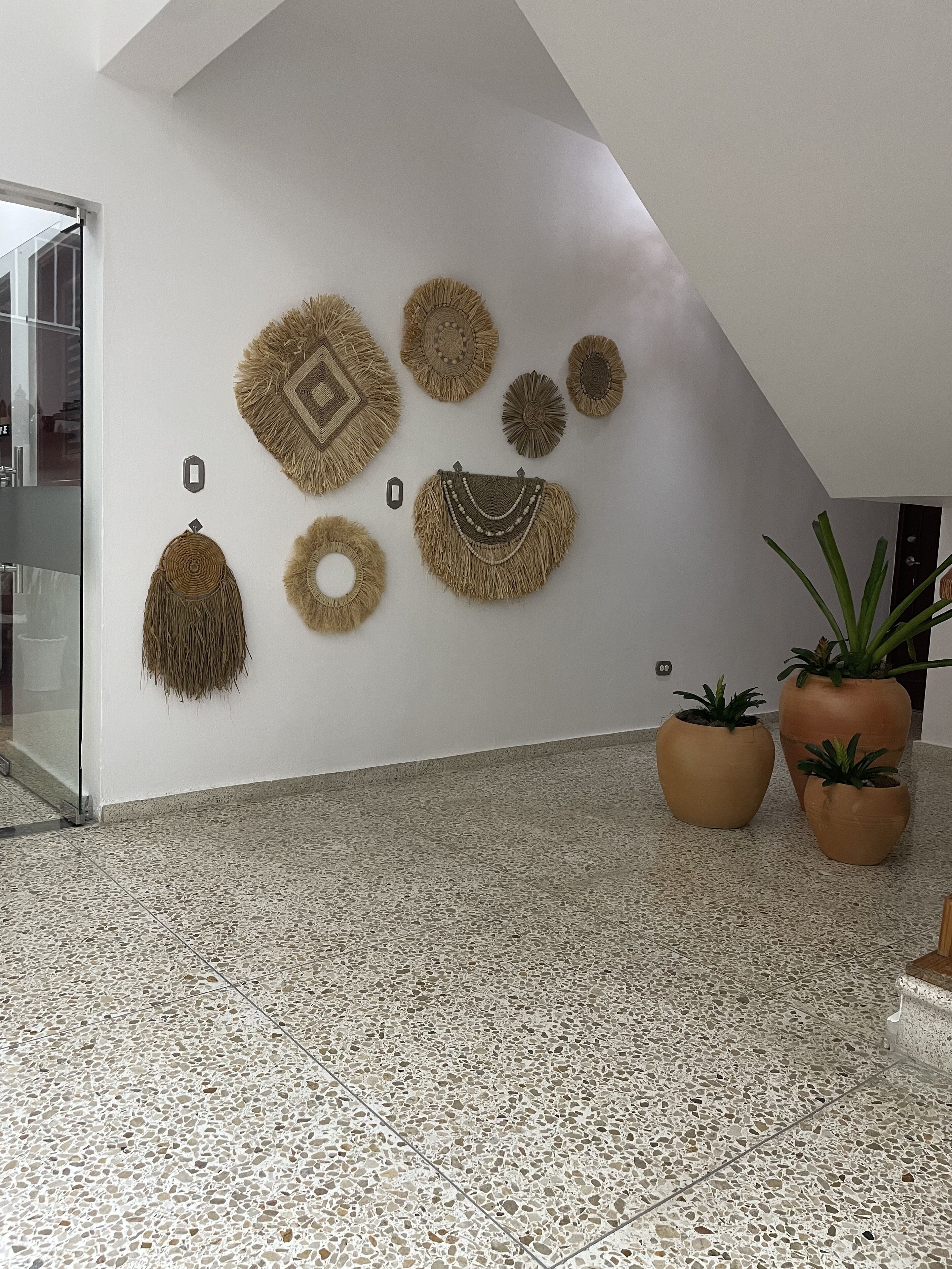 Un intérieur moderne avec un mur blanc orné de diverses tapisseries murales tissées, un sol en terrazzo et des plantes en pot.