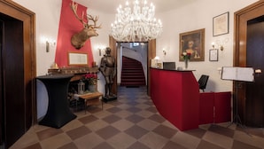 A lobby with a red reception desk, a chandelier, a deer head mounted on the wall, and a staircase in the background. - Eventlocation & Hotel Schloss Neuburg (Obrigheim)