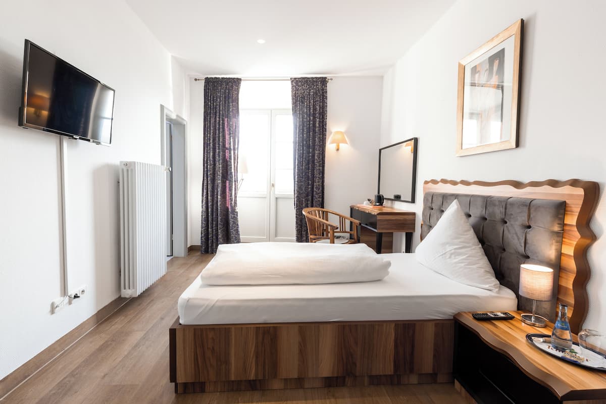 Ein modernes Hotelzimmer mit einem hölzernen Bett, einem Schreibtisch, einem Stuhl, einem Fernseher und einer Lampe.