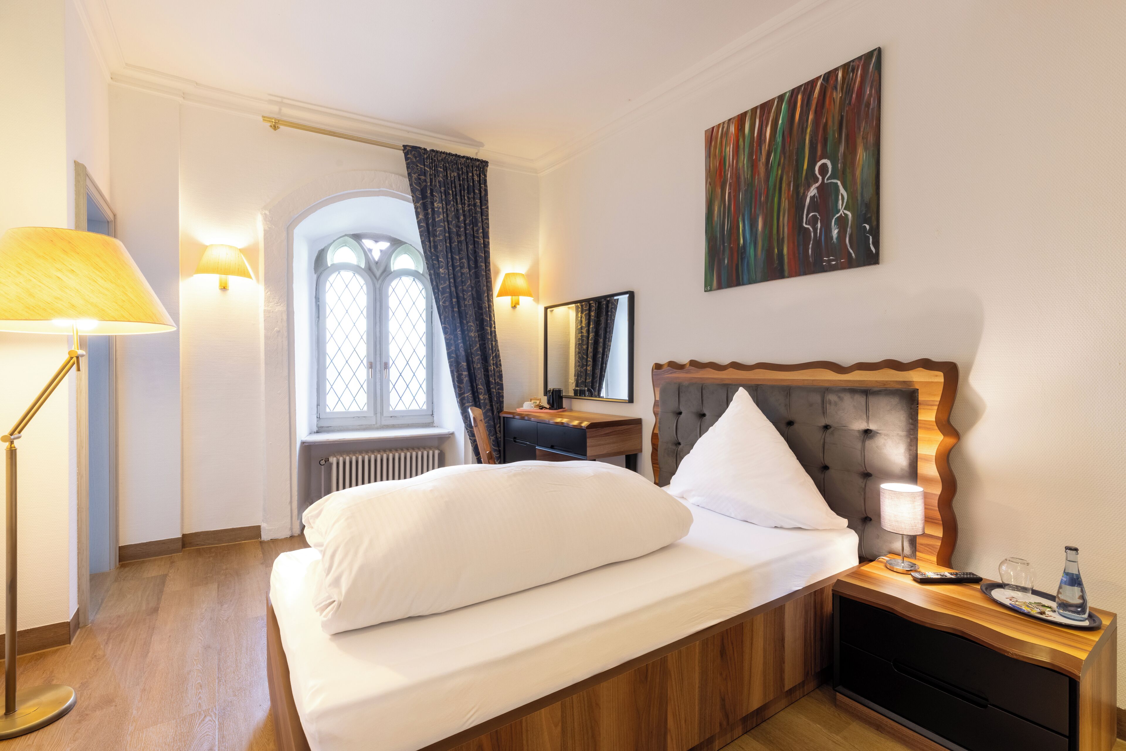 Una habitación de hotel con cama, mesita de noche, lámpara y un cuadro en la pared.