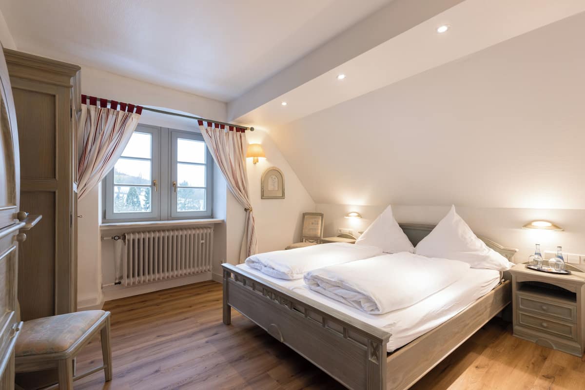 Ein Schlafzimmer mit einem hölzernen Bett, einem Heizkörper, einem Fenster mit Vorhängen und einem Nachttisch mit Lampe.