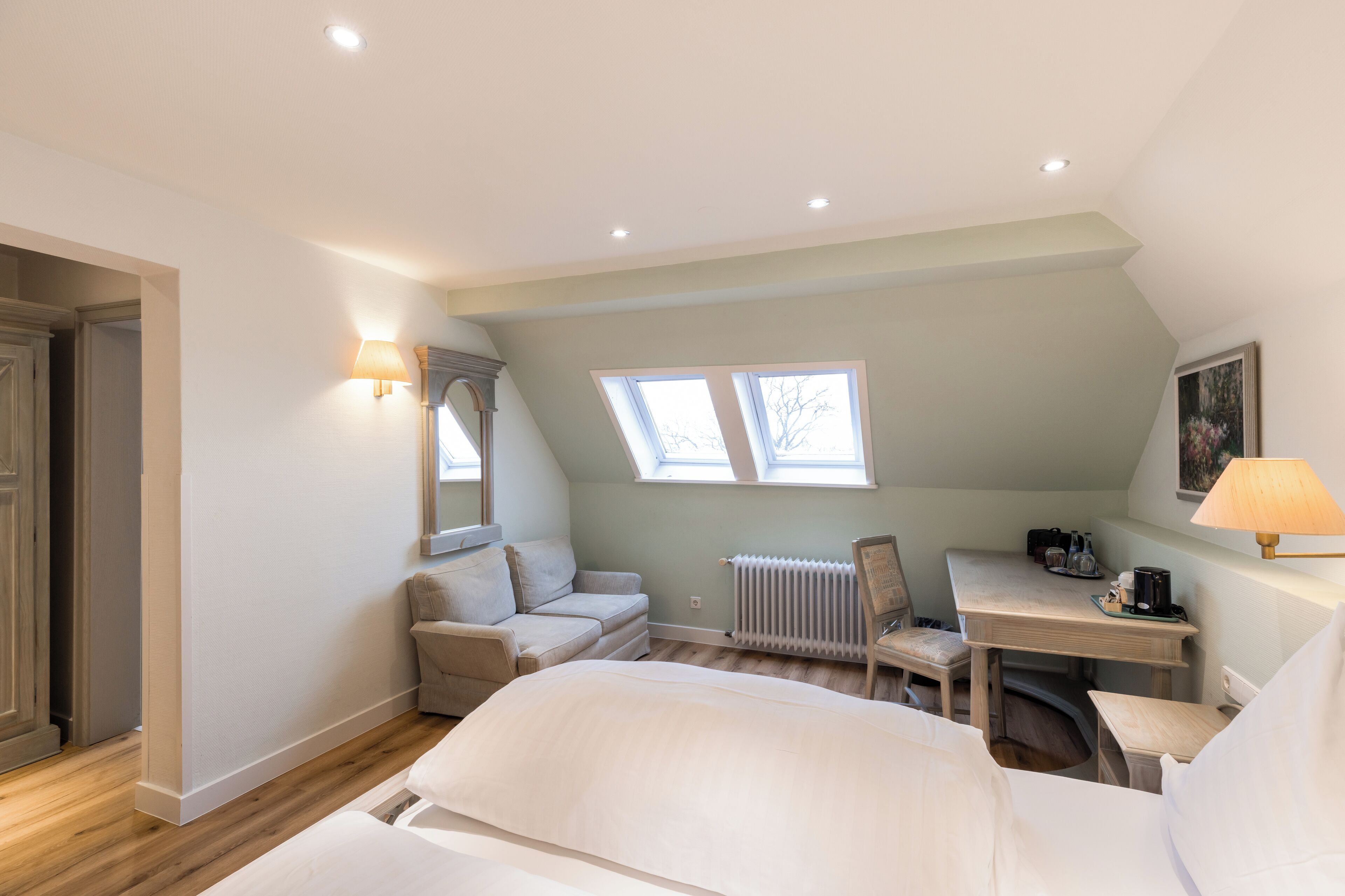 Un dormitorio con cama, escritorio, silla, radiador y tragaluces.