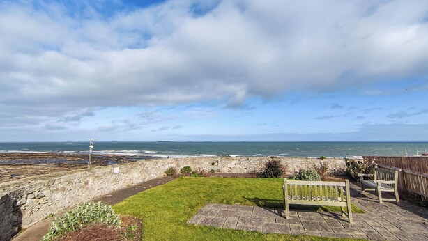 A coastal view with a grassy area, a wooden bench, and a stone wall. - Marram at the Viking (Seahouses)