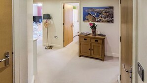 A hallway with a wooden cabinet, a floor lamp, and a framed picture on the wall. - Marram at the Viking (Seahouses)