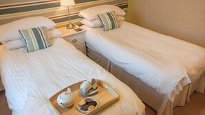 Two single beds with white linens and striped pillows, a bedside table with a lamp, and a tray with a teapot, cups, and cookies. - Marram at the Viking (Seahouses)