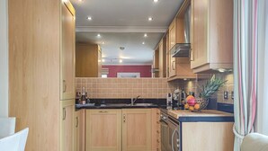A compact kitchen with wooden cabinets, a black countertop, and a tiled backsplash. - Marram at the Viking (Seahouses)