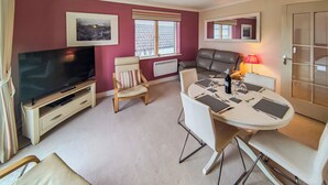 A living room with a television, a sofa, a dining table with chairs, and a fireplace. - Marram at the Viking (Seahouses)
