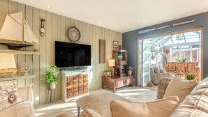 A living room with a television, wooden cabinets, a sailboat model, and a cozy seating area. - A fabulous seaside retreat, ideal for couples, friends, or small families. (Hayling Island)