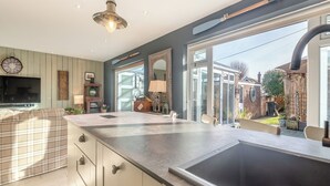 A modern kitchen with a large island, a built-in oven, and a large window overlooking a garden. - A fabulous seaside retreat, ideal for couples, friends, or small families. (Hayling Island)