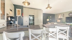 A modern kitchen with a central island, white cabinetry, and pendant lighting. - A fabulous seaside retreat, ideal for couples, friends, or small families. (Hayling Island)