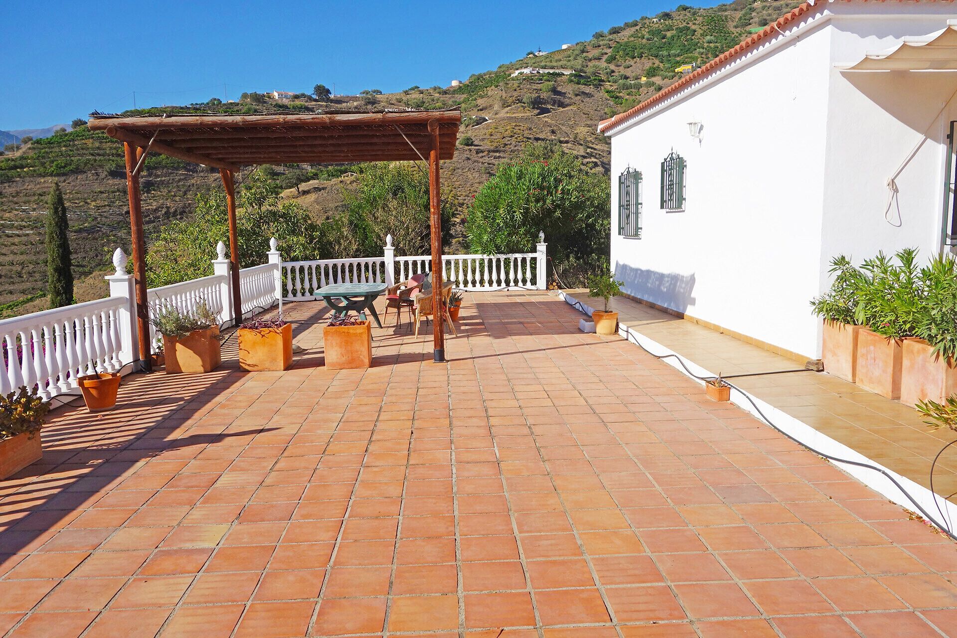 A terrace with a pergola, outdoor seating, and potted plants.