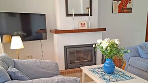 Un salon comprenant un canapé, une table basse avec un vase, une cheminée et un téléviseur fixé au mur.