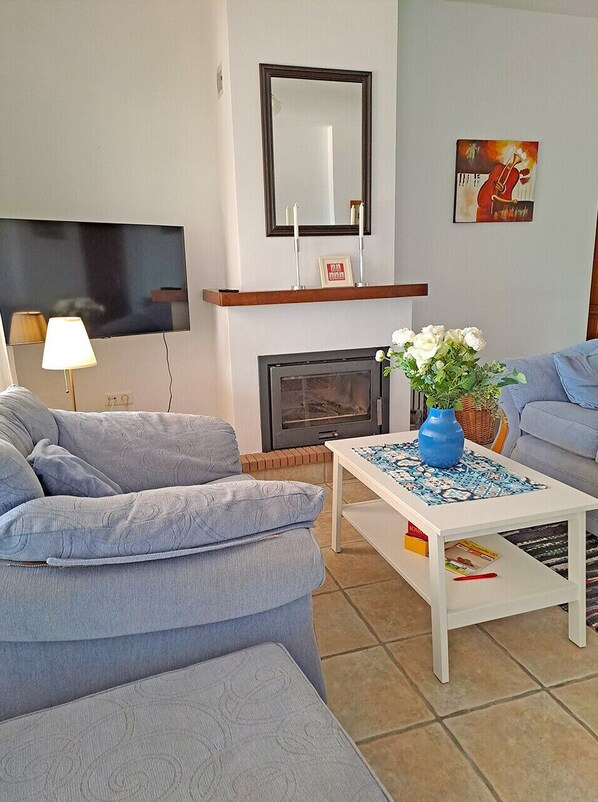 A living room with a sofa, a coffee table with a vase, a fireplace, and a TV mounted on the wall.