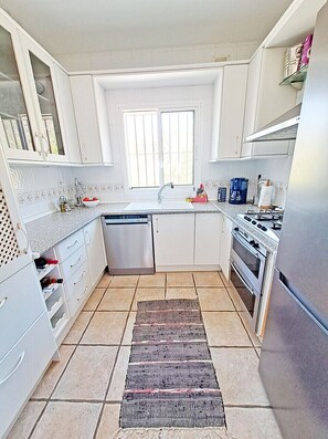 A modern kitchen with white cabinets, a dishwasher, an oven, a stove, and a window above the sink.