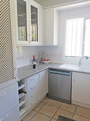 A compact kitchen with white cabinets, a dishwasher, and a window providing natural light. - Villa Sinsonte (Torrox)