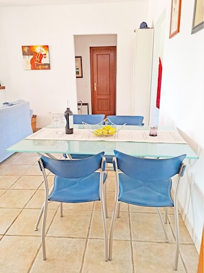 A dining area with a glass table, blue chairs, a wine bottle, and a bowl of lemons. - Villa Sinsonte (Torrox)