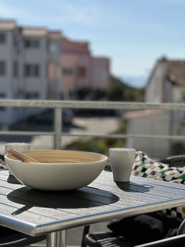 A table with a bowl, a spoon, and a cup, set against a backdrop of buildings and a clear sky.