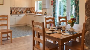 A kitchen with white cabinets, a sink, and a window with curtains. There is a dining table with chairs and a vase of flowers. - Picked for its character and only a 5 minute drive to the beach. (Keeston)