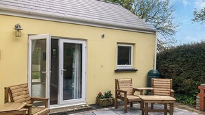 A yellow building with a tiled patio, wooden furniture, and a sliding glass door. - Picked for its character and only a 5 minute drive to the beach. (Keeston)
