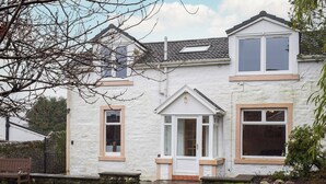 A two-story house with a white exterior, a front porch, and a small garden. - 3 bedroom accommodation in Dunoon (Dunoon)