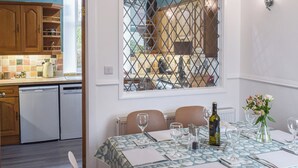 A dining area with a table set for four, a window with a metal grid, and a kitchen in the background. - 3 bedroom accommodation in Dunoon (Dunoon)