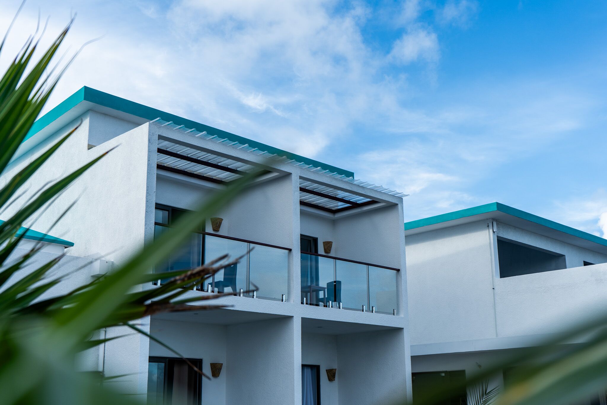 A modern two-story building with a flat roof, large windows, and a balcony with glass railings.