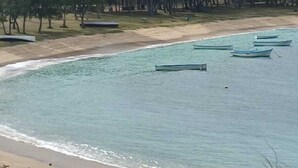 Ett kustområde med en sandstrand, flera båtar och en samling byggnader på en kulle i bakgrunden.