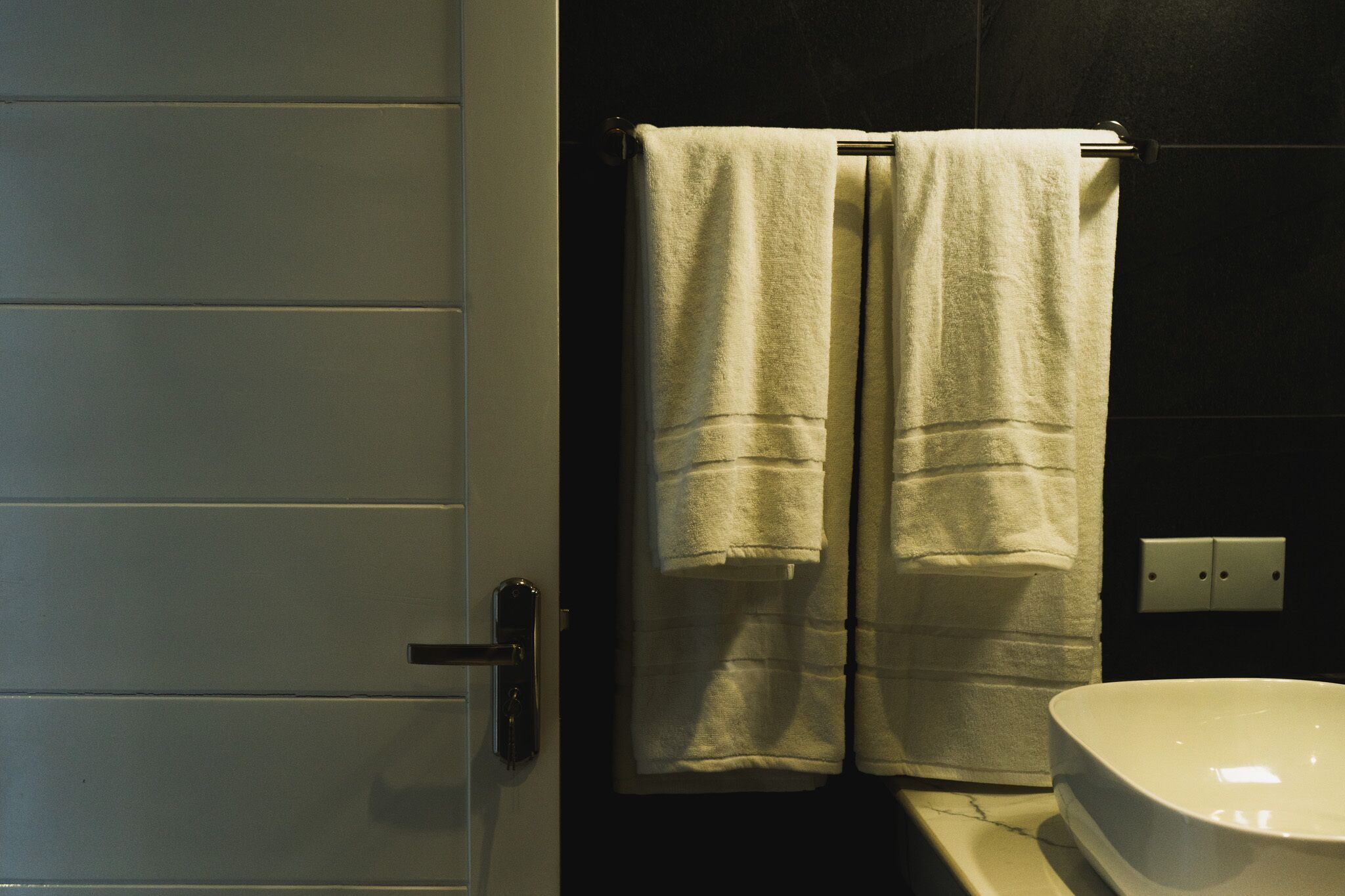 A bathroom with a white bathtub, a towel rack with two towels, and a door with a handle.