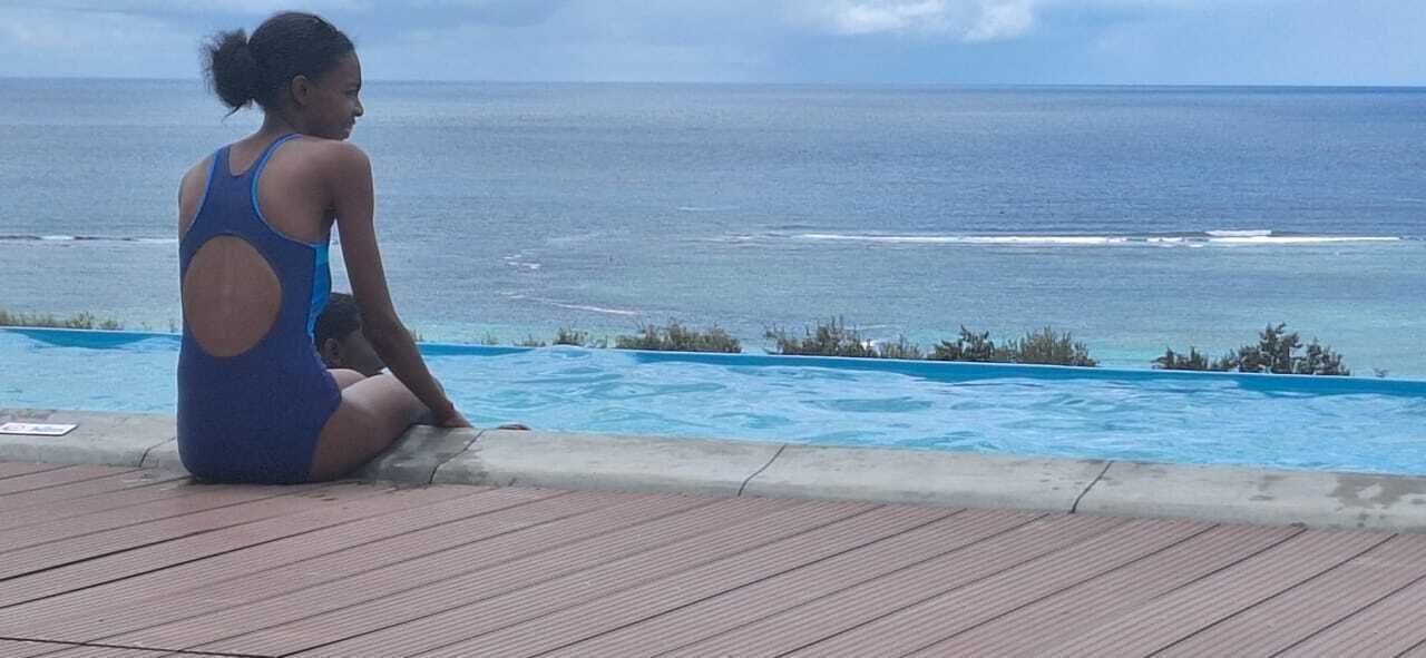 A person sitting by a pool with a view of the ocean.