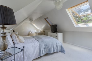 A bedroom with a bed, a TV, a lamp, and a window with a view of greenery.