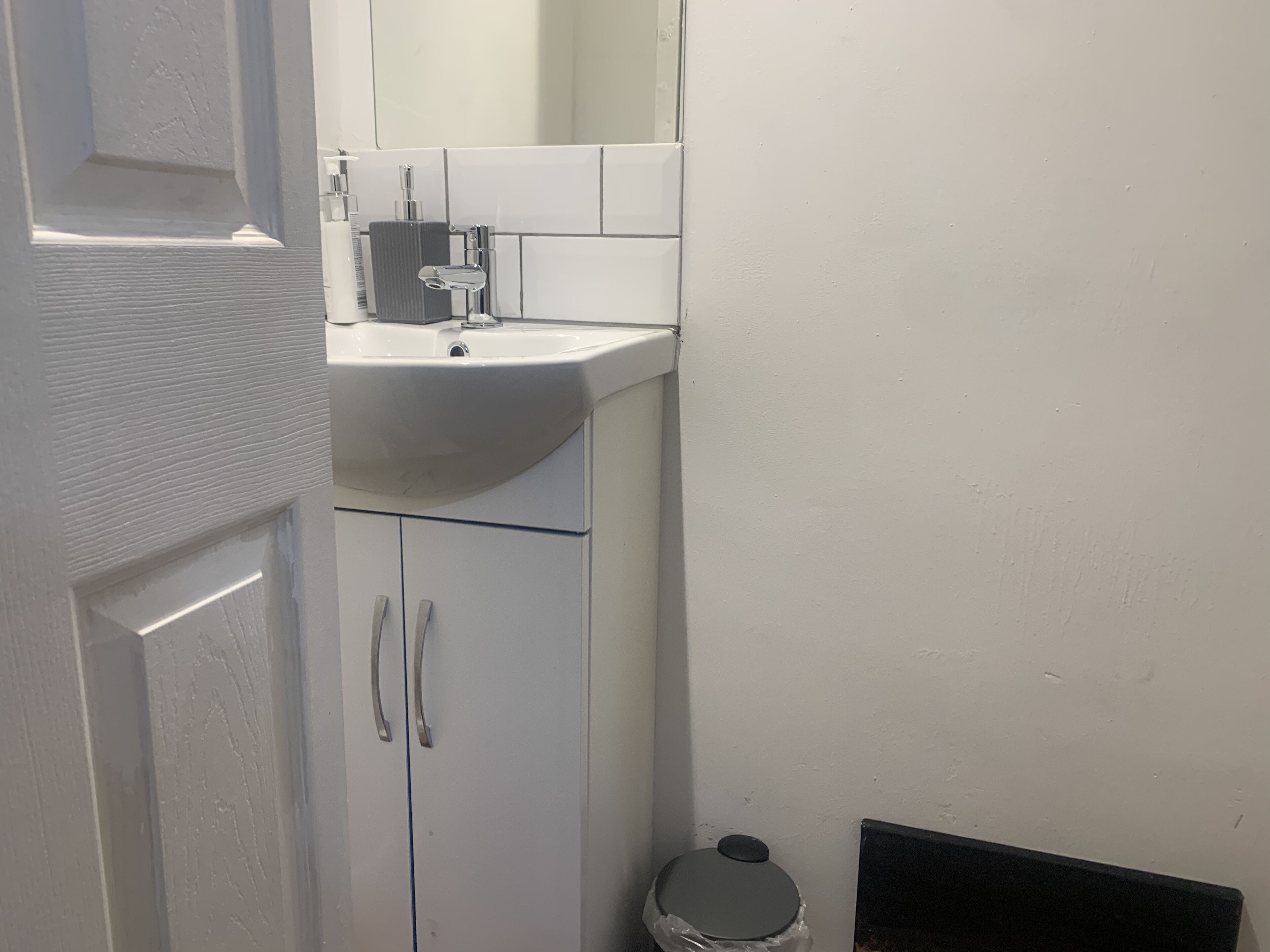 A bathroom with a white sink, a mirror, and a trash bin.