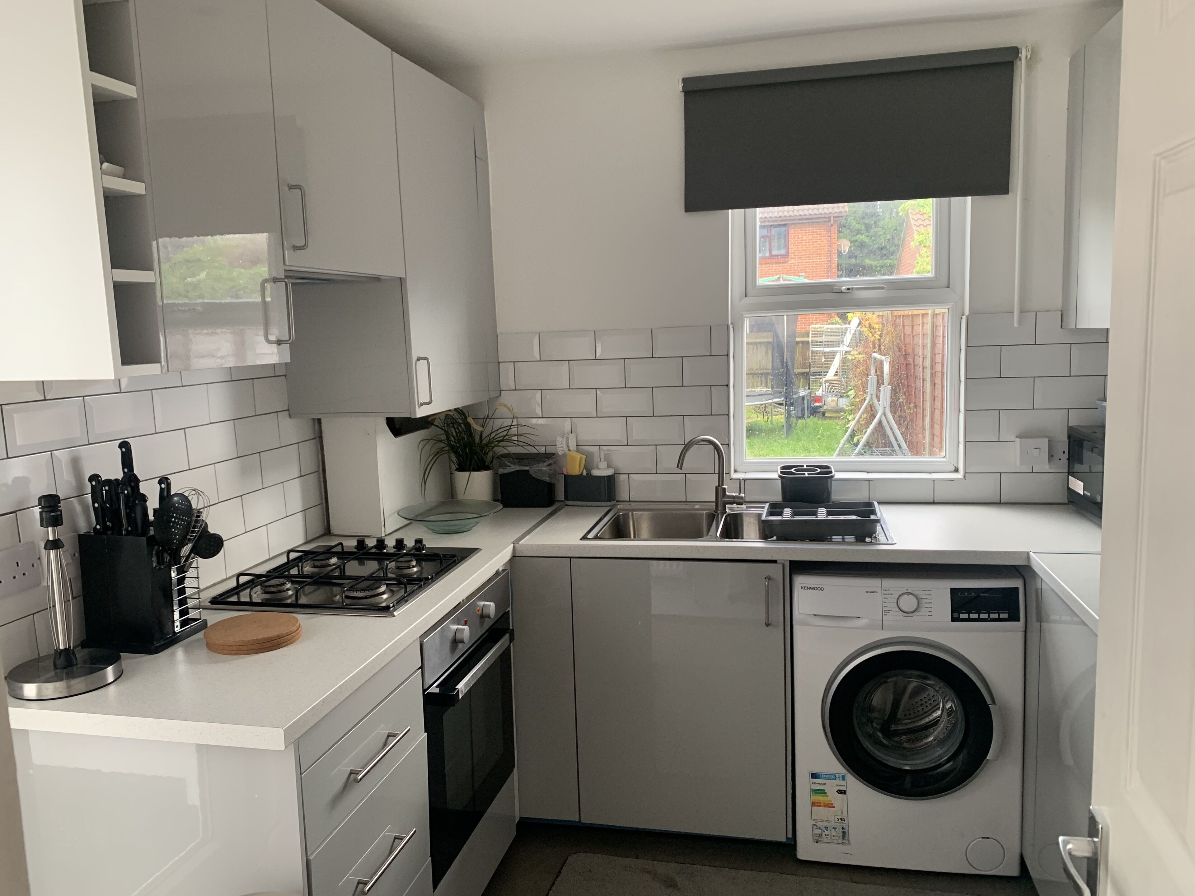 A compact kitchen with white cabinets, a gas stove, a sink, and a built-in washing machine.