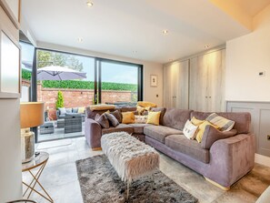 A modern living room with a large sectional sofa, a fluffy ottoman, and a dining area with wicker furniture.