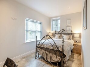 A bedroom with a four-poster bed, two bedside tables, a chair, and two windows with blinds.