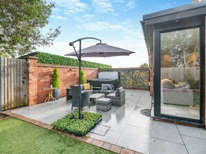 Un patio con mobiliario exterior, una parrilla y un mural en la pared.